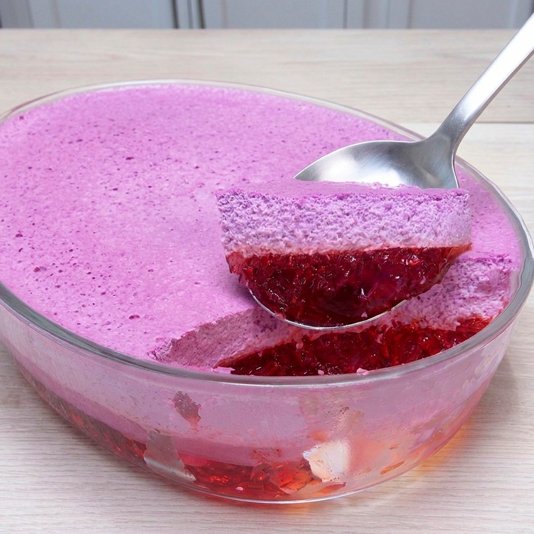 Two-layer berry gelatin mousse dessert in a glass bowl with a spoon lifting out a portion showing jelly and mousse layers